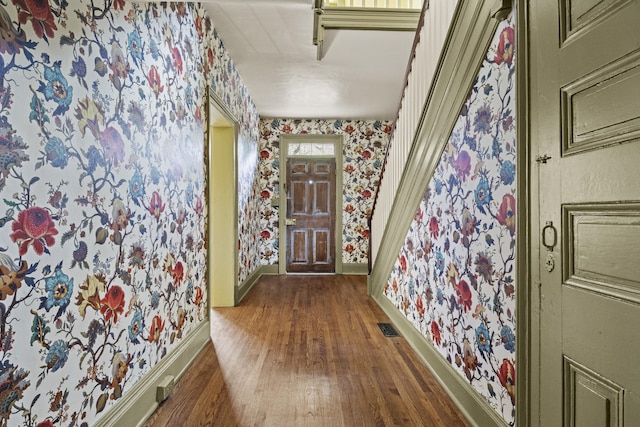 hallway with wallpapered walls, wood finished floors, visible vents, and baseboards