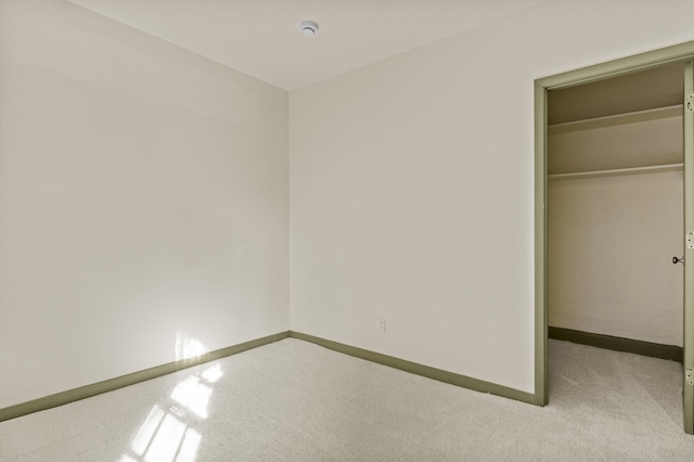 unfurnished bedroom with a walk in closet, a closet, carpet flooring, and baseboards
