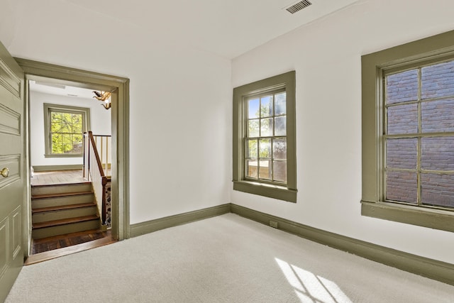 carpeted spare room with baseboards, visible vents, and stairway