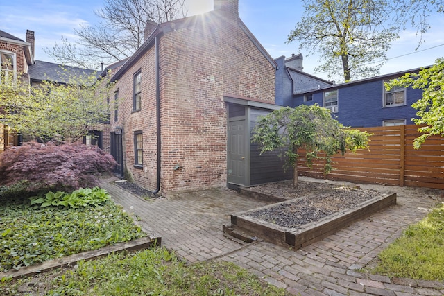 rear view of property featuring a garden, a chimney, fence, brick siding, and a patio area