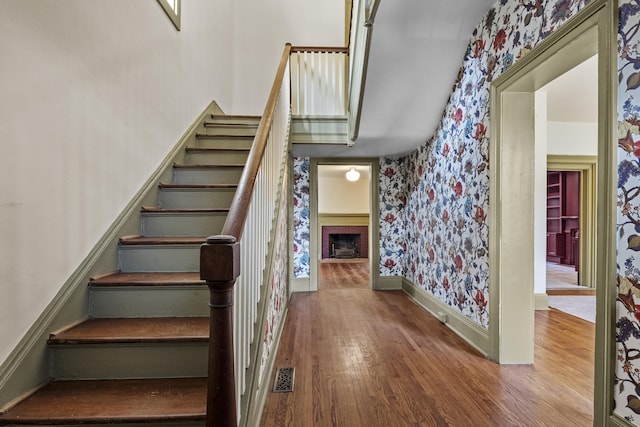 stairs with visible vents, baseboards, wallpapered walls, wood finished floors, and a fireplace