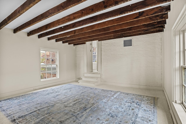 empty room featuring brick wall, beam ceiling, and carpet