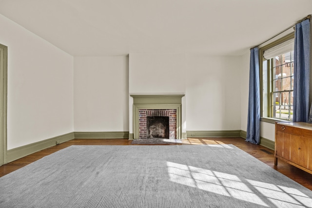 unfurnished living room featuring a brick fireplace, wood finished floors, visible vents, and baseboards