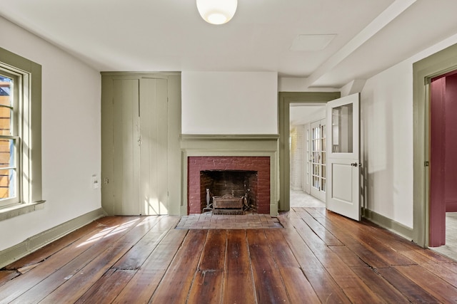 unfurnished living room featuring baseboards, hardwood / wood-style flooring, and a brick fireplace