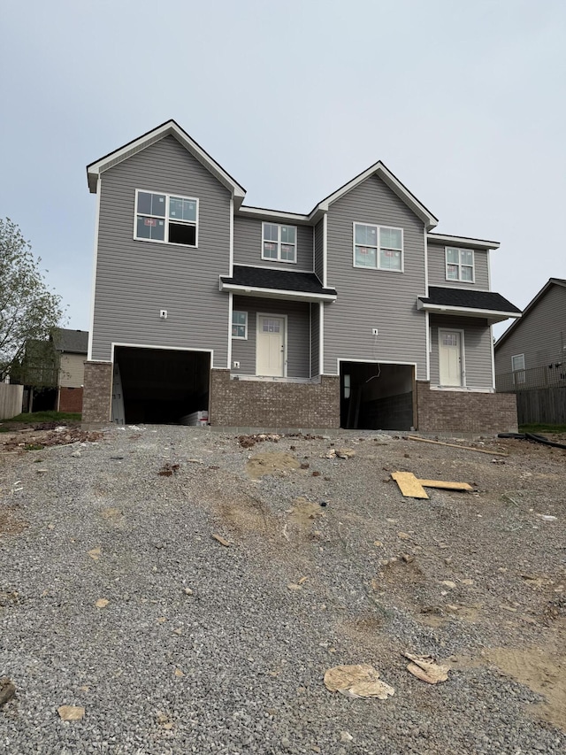 view of front of home with brick siding, an attached garage, and gravel driveway