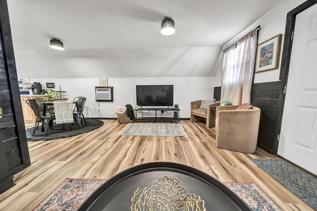 living area featuring wood finished floors, a wall unit AC, and vaulted ceiling