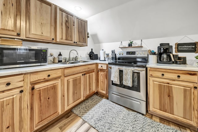 kitchen featuring a sink, light wood-style floors, stainless steel appliances, light countertops, and vaulted ceiling