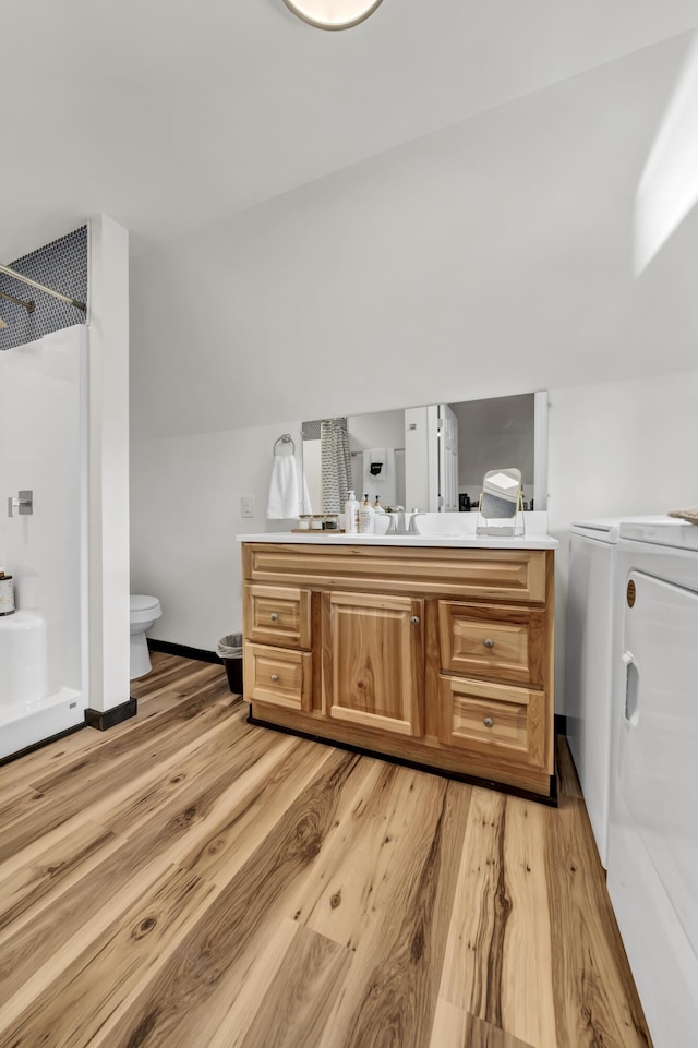 bathroom with wood finished floors, toilet, vanity, washing machine and dryer, and a shower