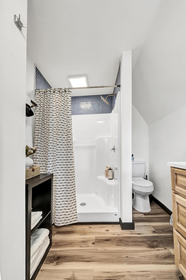 bathroom with lofted ceiling, curtained shower, toilet, wood finished floors, and vanity