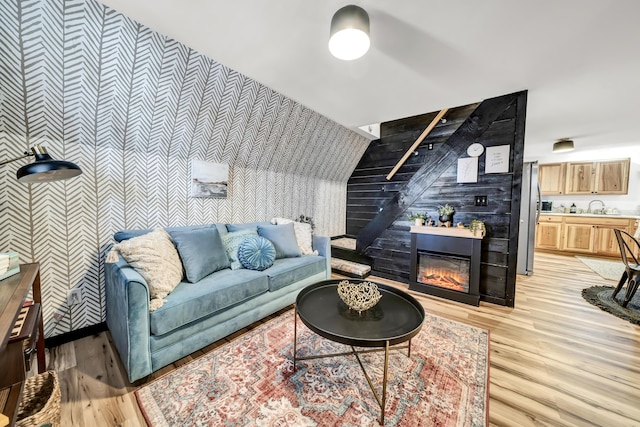 living room with wallpapered walls, a fireplace, light wood finished floors, and an accent wall