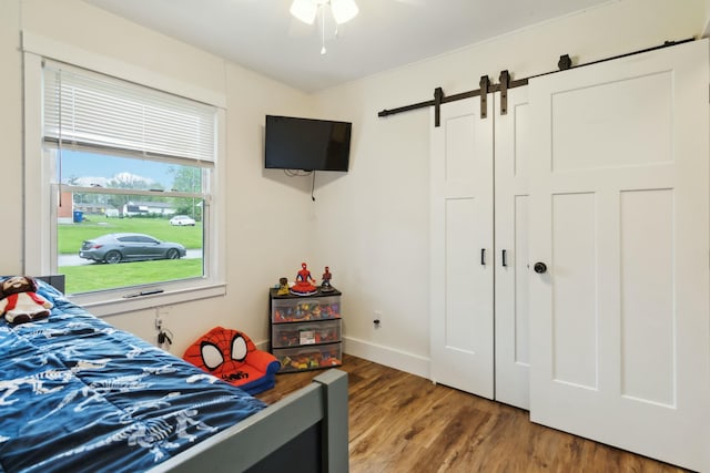 bedroom with baseboards, wood finished floors, and a barn door