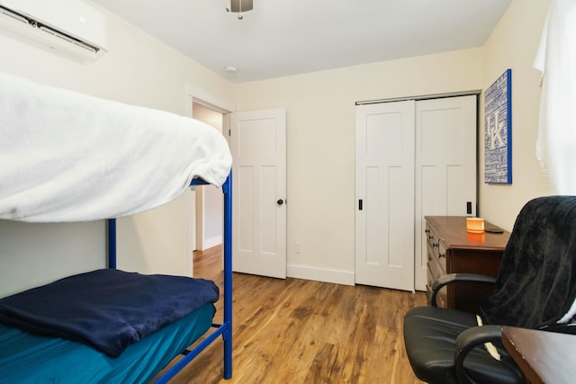 bedroom featuring baseboards, a ceiling fan, wood finished floors, a closet, and a wall mounted AC