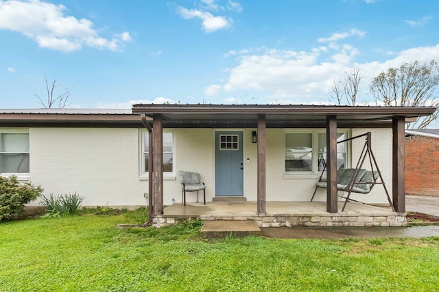 rear view of property with a lawn, brick siding, and covered porch