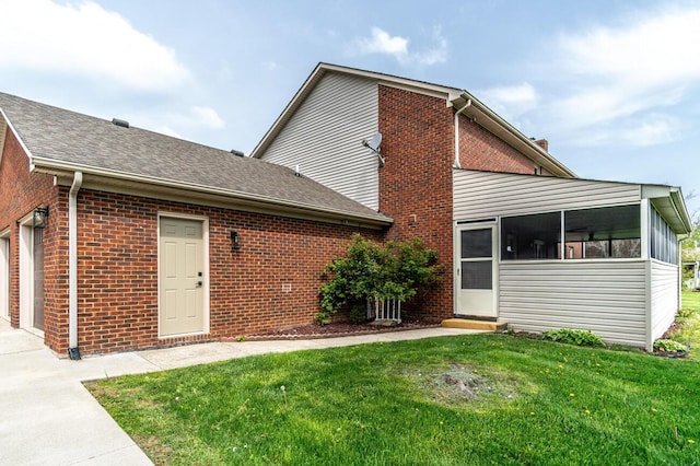 back of property with brick siding, a sunroom, driveway, and a lawn