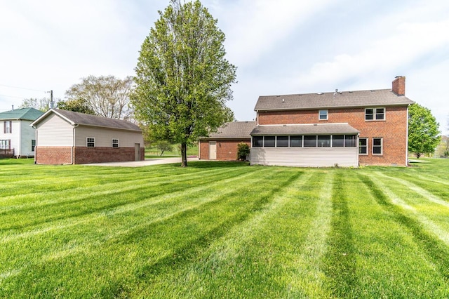 rear view of house with brick siding, a sunroom, a chimney, and a lawn
