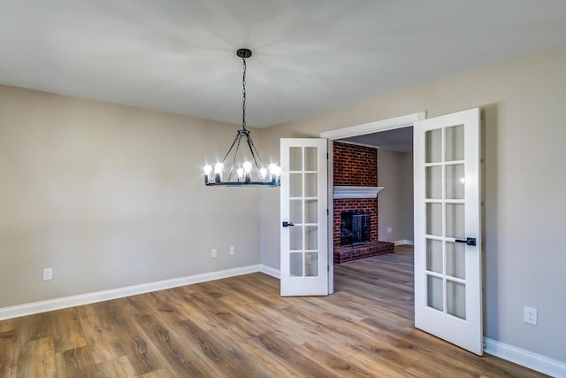 unfurnished dining area with wood finished floors, french doors, baseboards, a fireplace, and a notable chandelier