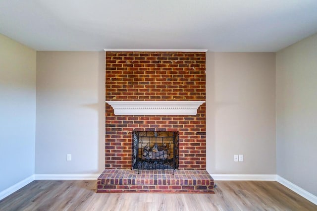 unfurnished living room featuring wood finished floors, a brick fireplace, and baseboards
