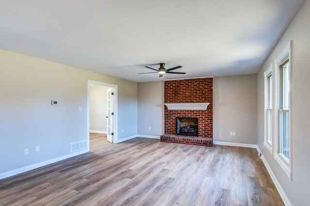 unfurnished living room with baseboards, visible vents, wood finished floors, ceiling fan, and a fireplace