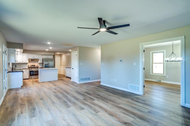 unfurnished living room with ceiling fan with notable chandelier, baseboards, and visible vents