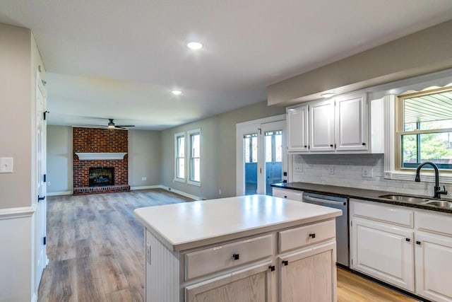 kitchen with a ceiling fan, stainless steel dishwasher, a sink, light wood-style flooring, and tasteful backsplash