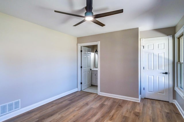 unfurnished bedroom with ensuite bathroom, baseboards, visible vents, wood finished floors, and ceiling fan