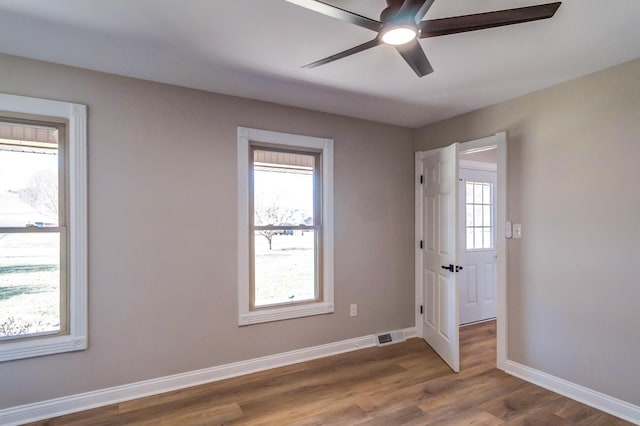 empty room with wood finished floors, visible vents, a ceiling fan, and baseboards