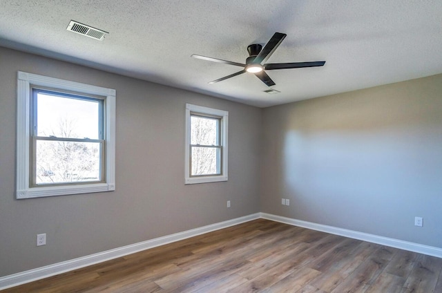 spare room with wood finished floors, visible vents, a textured ceiling, and ceiling fan