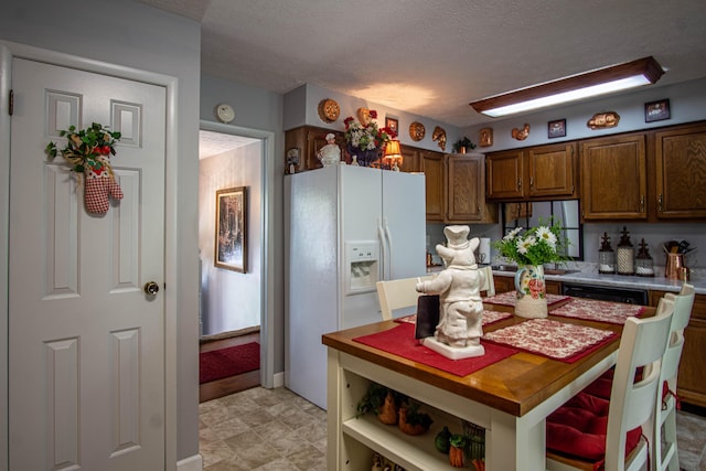 kitchen featuring a textured ceiling, freestanding refrigerator, white refrigerator with ice dispenser, brown cabinetry, and light countertops