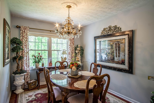 dining room with wood finished floors, baseboards, a textured ceiling, and a notable chandelier