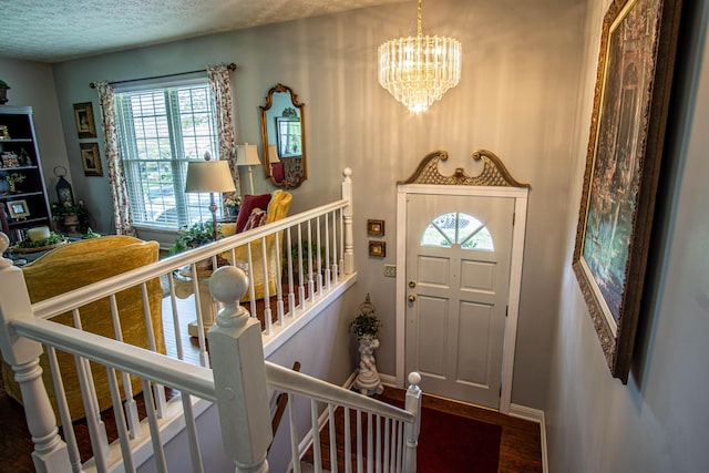 entryway featuring a textured ceiling, wood finished floors, a healthy amount of sunlight, and an inviting chandelier