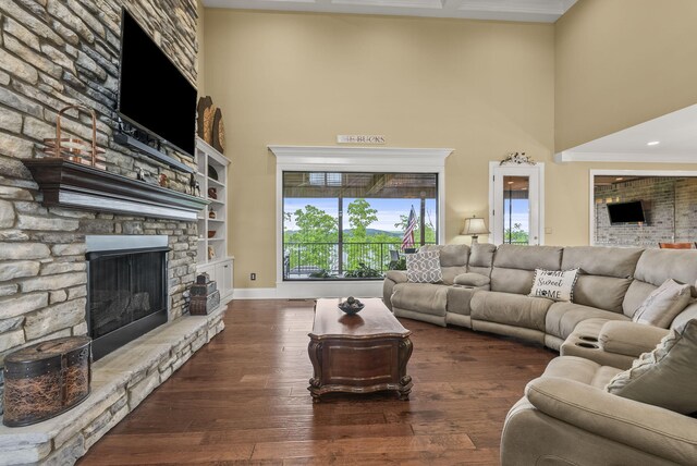 living room with a towering ceiling, a stone fireplace, wood-type flooring, and baseboards