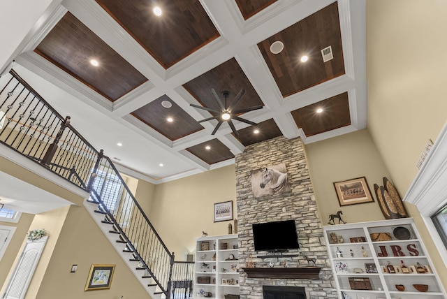 living room featuring coffered ceiling, a towering ceiling, a stone fireplace, beam ceiling, and a ceiling fan