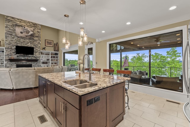 kitchen with a sink, a stone fireplace, a breakfast bar, light tile patterned floors, and pendant lighting