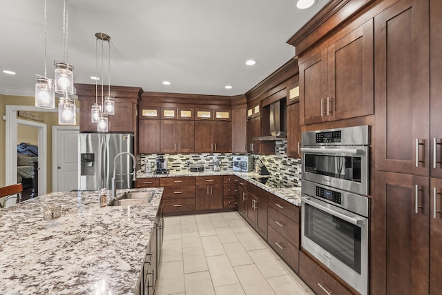 kitchen with a sink, appliances with stainless steel finishes, wall chimney exhaust hood, backsplash, and glass insert cabinets