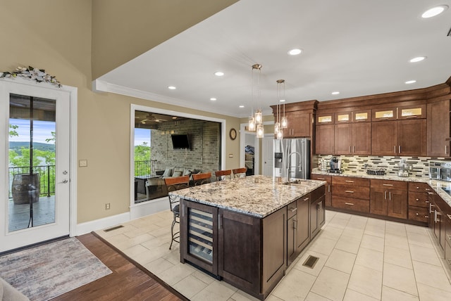 kitchen with tasteful backsplash, a sink, healthy amount of natural light, a kitchen island with sink, and crown molding