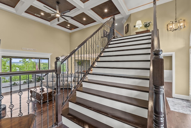 staircase featuring a high ceiling, wood finished floors, ceiling fan, coffered ceiling, and beamed ceiling