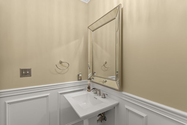 bathroom featuring wainscoting, a decorative wall, and a sink