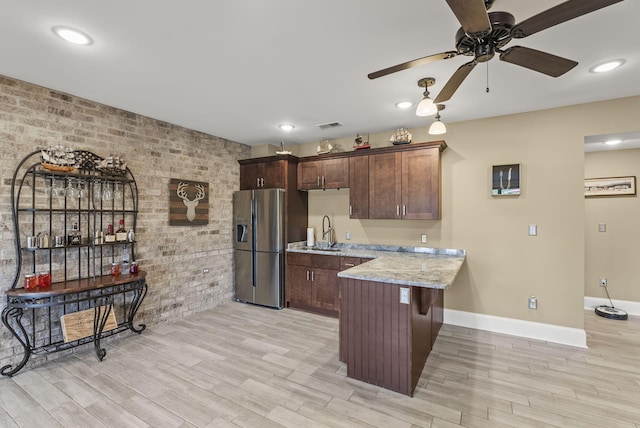 kitchen with stainless steel fridge, a sink, a peninsula, brick wall, and light wood-type flooring