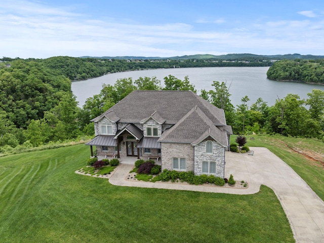 craftsman-style house with a water view, a standing seam roof, stone siding, driveway, and a front lawn