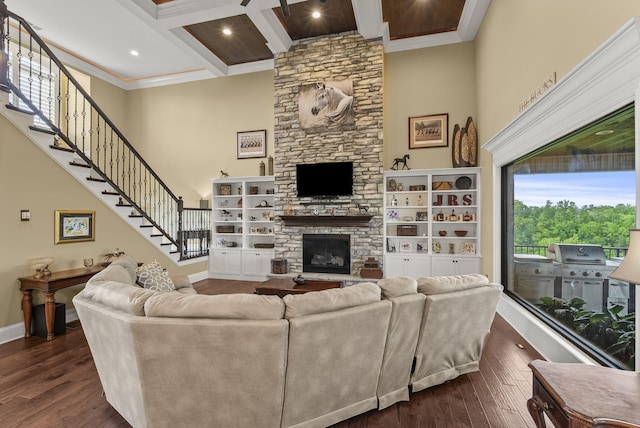 living area featuring a high ceiling, ornamental molding, a stone fireplace, beam ceiling, and dark wood-style flooring