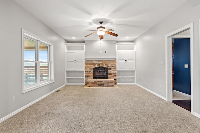 unfurnished living room featuring carpet floors, a stone fireplace, baseboards, and ceiling fan