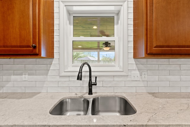 kitchen with brown cabinetry, backsplash, light stone counters, and a sink