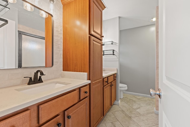 bathroom with toilet, a sink, baseboards, decorative backsplash, and two vanities