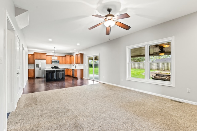unfurnished living room featuring dark colored carpet, a healthy amount of sunlight, a ceiling fan, and visible vents