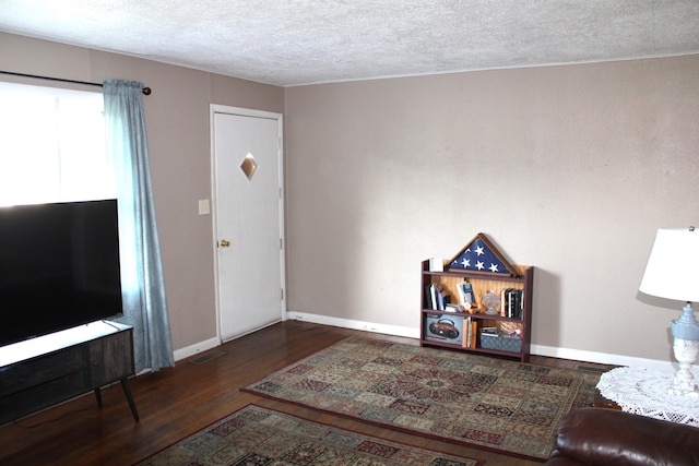 living area featuring a textured ceiling, wood finished floors, and baseboards