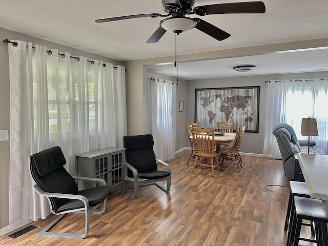 dining room featuring a textured ceiling, visible vents, baseboards, wood finished floors, and a ceiling fan