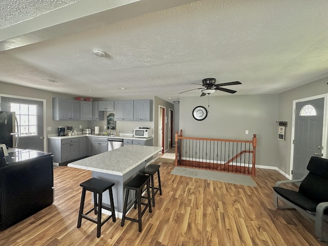 kitchen with white microwave, light wood-style flooring, light countertops, gray cabinetry, and dishwasher