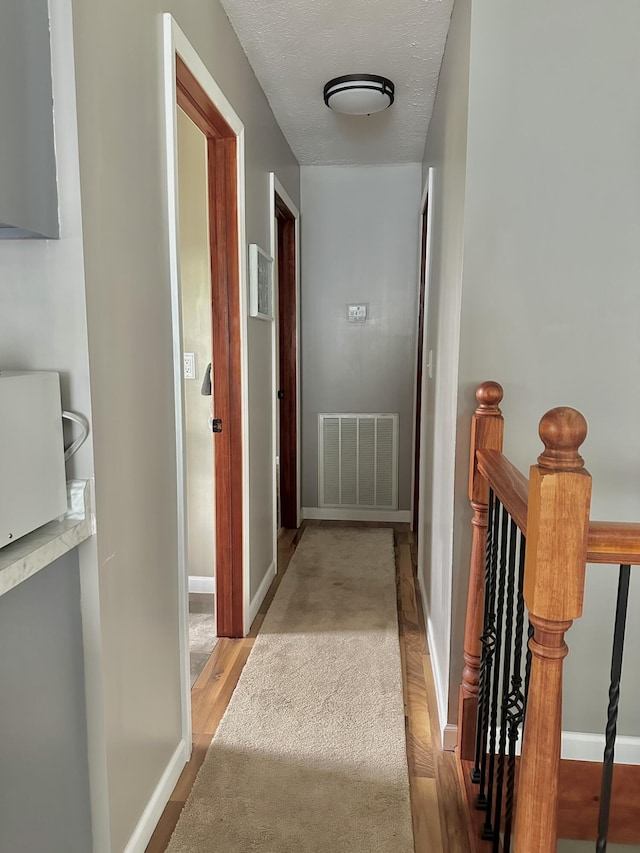 hallway with an upstairs landing, visible vents, wood finished floors, and baseboards