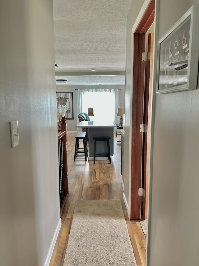 hall with a textured ceiling, an upstairs landing, wood finished floors, and baseboards