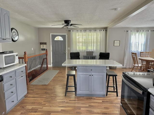 kitchen featuring a textured ceiling, a breakfast bar area, black / electric stove, and white microwave